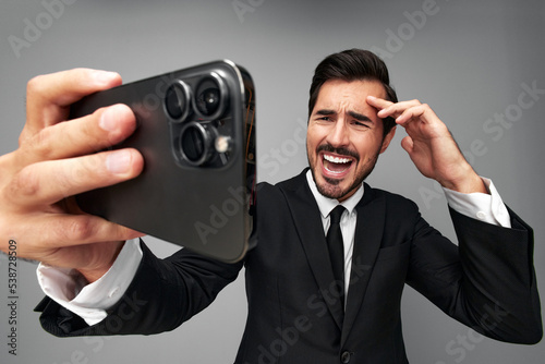 Man businessman holding the phone in his hand looking at him. Headache and anger from failure stress. Close-up wide angle photo gray isolated background