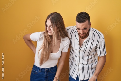 Young couple standing over yellow background suffering of backache, touching back with hand, muscular pain