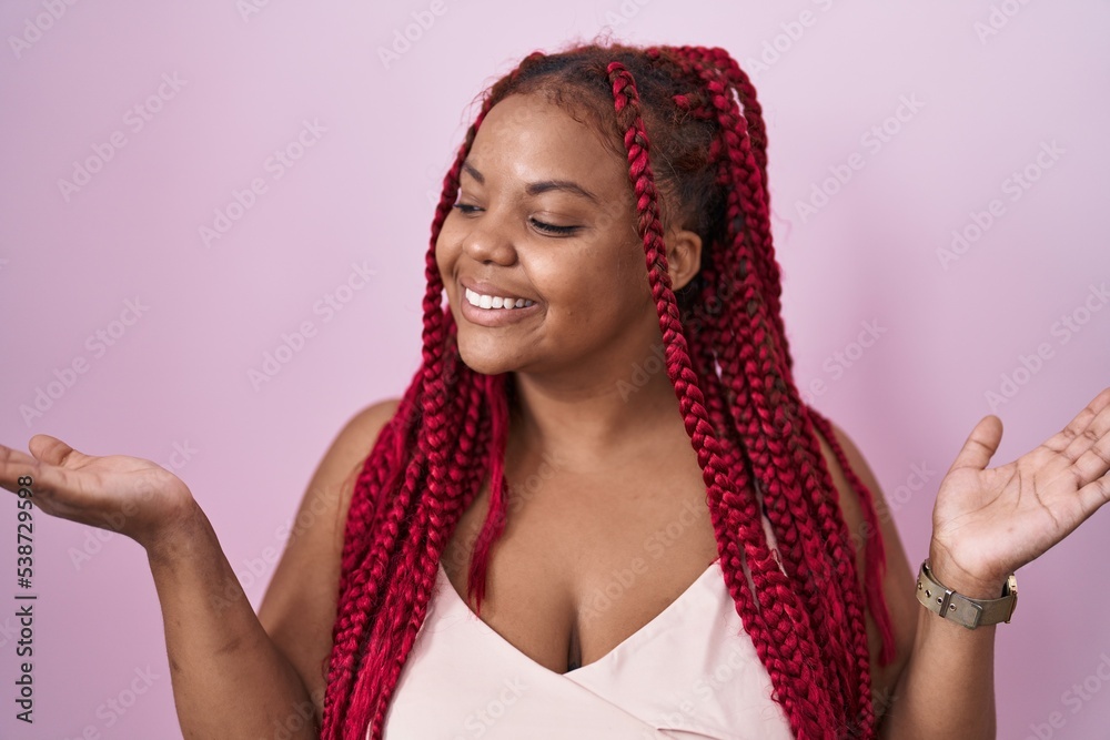 African american woman with braided hair standing over pink background smiling showing both hands open palms, presenting and advertising comparison and balance African american woman with braided hair standing over pink background smiling showing both hands open palms, presenting and advertising comparison and balance