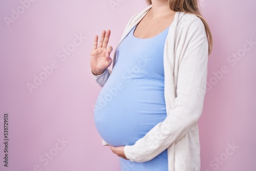 Young pregnant woman expecting a baby, touching pregnant belly doing ok sign with fingers, smiling friendly gesturing excellent symbol