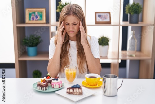 Young caucasian woman eating pastries t for breakfast with hand on head for pain in head because stress. suffering migraine.