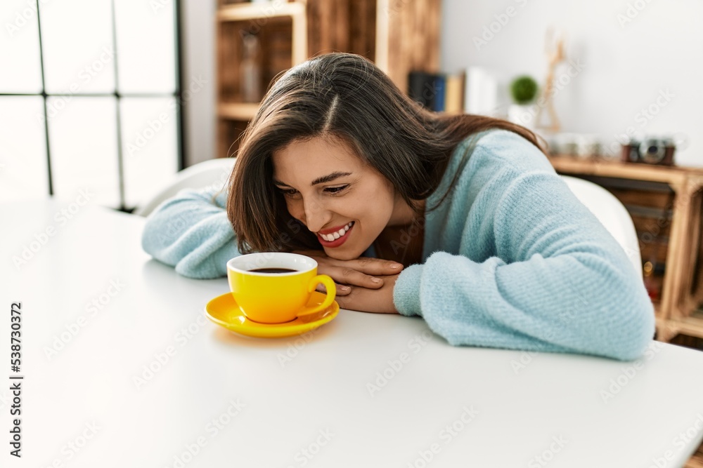 Young woman drinking coffee sitting on table at home Young woman drinking coffee sitting on table at home