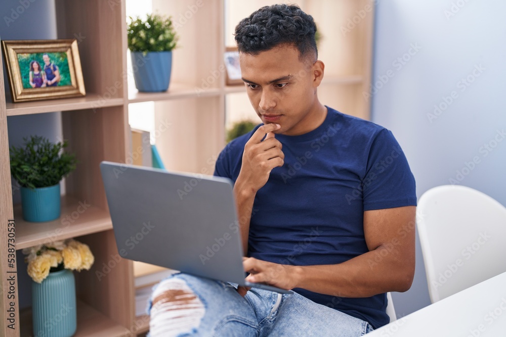 Young latin man using laptop sitting on table at home Young latin man using laptop sitting on table at home