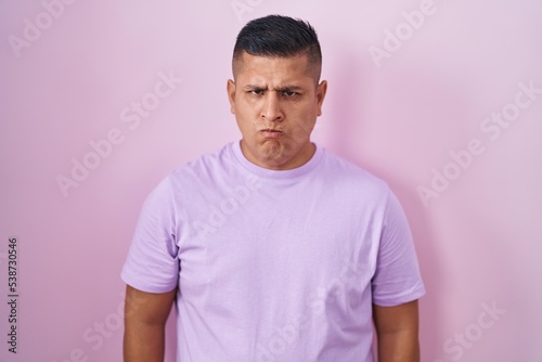 Young hispanic man standing over pink background skeptic and nervous, frowning upset because of problem. negative person.