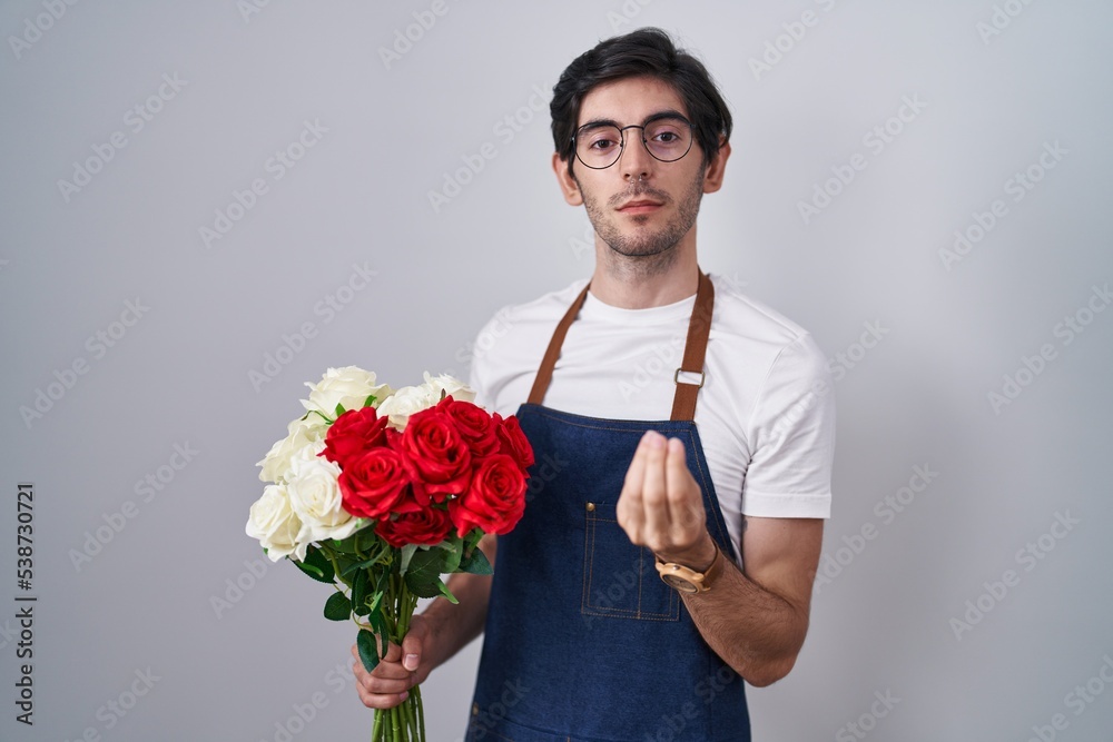 Young hispanic man holding bouquet of white and red roses doing italian gesture with hand and fingers confident expression