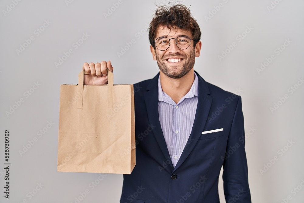 Hispanic business man holding delivery bag looking positive and happy standing and smiling with a confident smile showing teeth Hispanic business man holding delivery bag looking positive and happy standing and smiling with a confident smile showing teeth