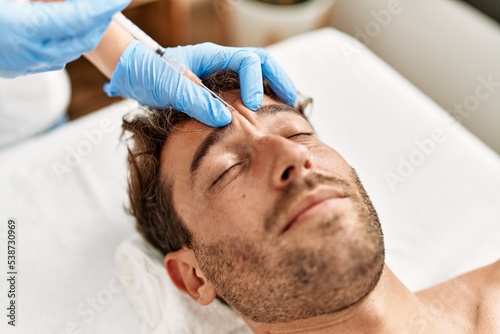 Young hispanic man having facial anti-aging treatment at beauty center