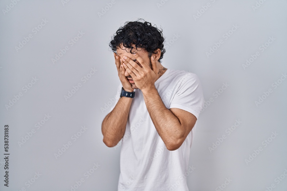 Hispanic man standing over isolated background with sad expression covering face with hands while crying. depression concept. Hispanic man standing over isolated background with sad expression covering face with hands while crying. depression concept.