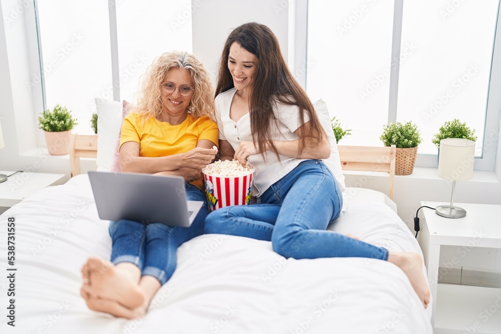 Two women mother and daughter watching movie on laptop at bedroom