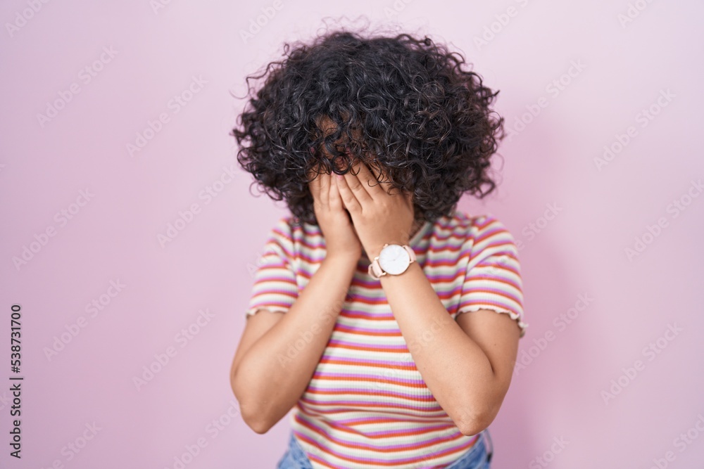 Young middle east woman standing over pink background with sad expression covering face with hands while crying. depression concept. Young middle east woman standing over pink background with sad expression covering face with hands while crying. depression concept.