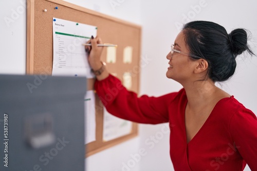 Young chinese woman business worker writing on cork board at office