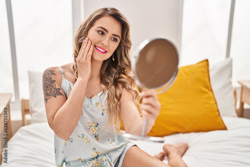 Young woman looking face on mirror sitting on bed at bedroom Young woman looking face on mirror sitting on bed at bedroom
