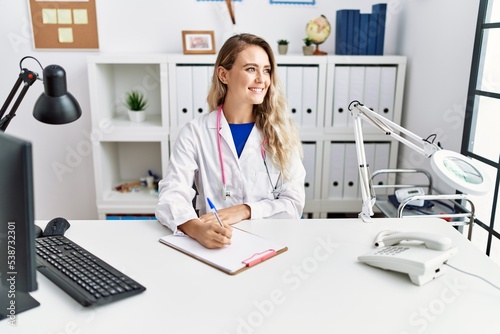 Young woman wearing doctor uniform writing on document at clinic