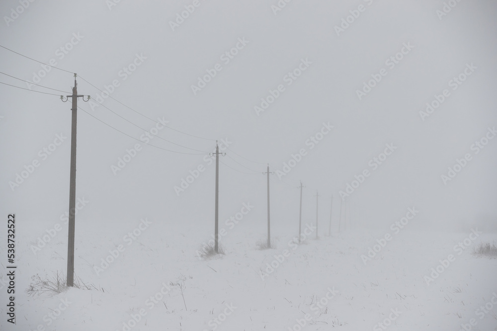 Poles with high-voltage wires extending into the distance in a snowy fog