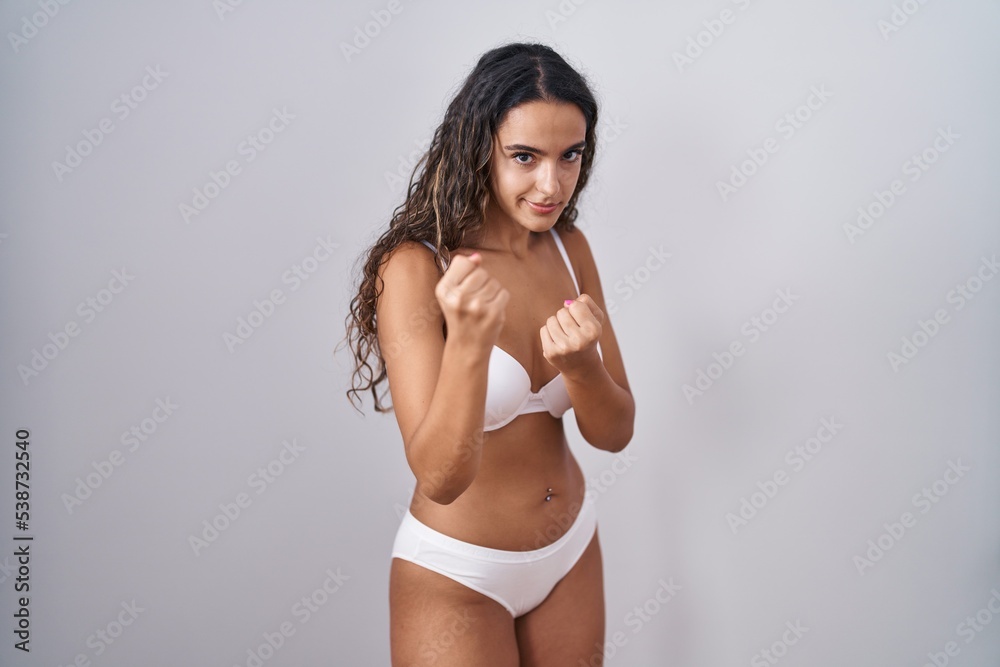 Young hispanic woman wearing white lingerie ready to fight with fist defense gesture, angry and upset face, afraid of problem Young hispanic woman wearing white lingerie ready to fight with fist defense gesture, angry and upset face, afraid of problem