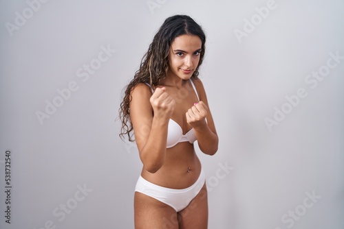 Young hispanic woman wearing white lingerie ready to fight with fist defense gesture, angry and upset face, afraid of problem