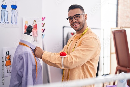 Young hispanic man tailor smiling confident measuring shirt at tailor shop