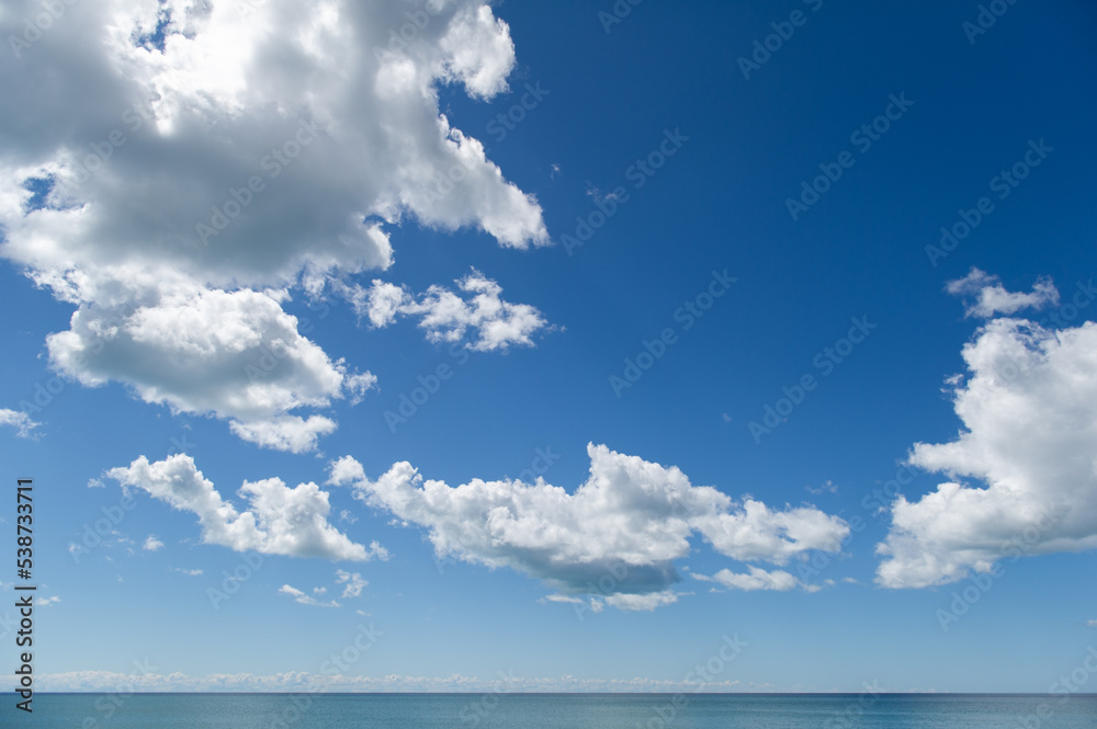 Fluffy white clouds over lake Ontario on a blue sky background.