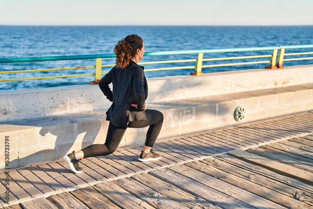 Middle age hispanic woman stretching legs at promenade