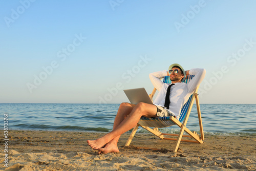 Photographie Happy man with laptop resting on deckchair near sea