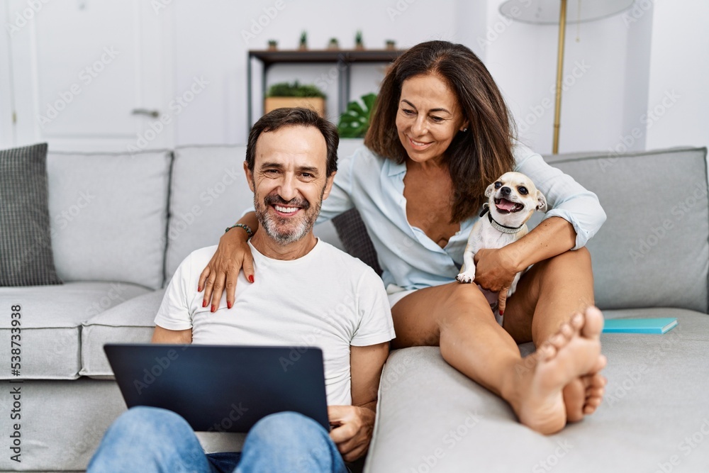 Middle age man and woman couple using laptop sitting on sofa with chihuahua at home Middle age man and woman couple using laptop sitting on sofa with chihuahua at home