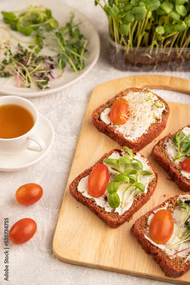 Red beet bread sandwiches with cream cheese, tomatoes and microgreen on gray. side view, selective focus. Red beet bread sandwiches with cream cheese, tomatoes and microgreen on gray. side view, selective focus.