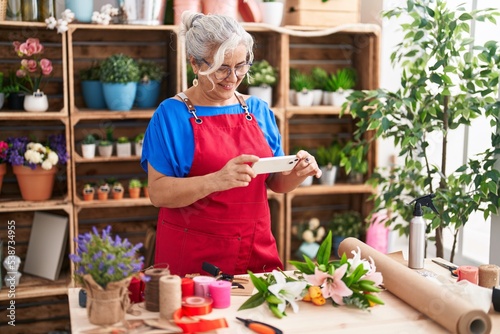 Middle age grey-haired woman florist make photo to flowers by smartphone at florist