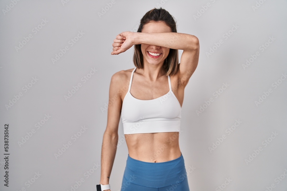 Hispanic woman wearing sportswear over isolated background covering eyes with arm smiling cheerful and funny. blind concept. Hispanic woman wearing sportswear over isolated background covering eyes with arm smiling cheerful and funny. blind concept.