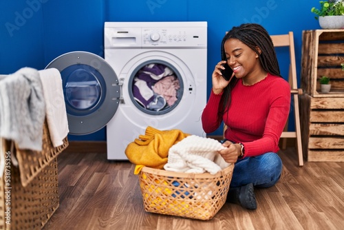 African american woman talking on smartphone washing clothes at laundry room