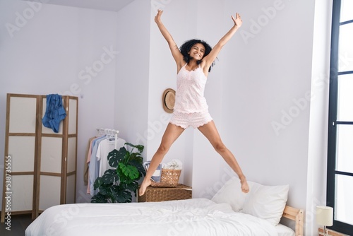 Young hispanic woman smiling confident jumping on bed at bedroom