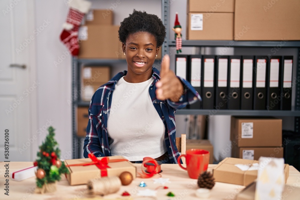 Fototapeta premium African american woman working at small business doing christmas decoration smiling friendly offering handshake as greeting and welcoming. successful business.