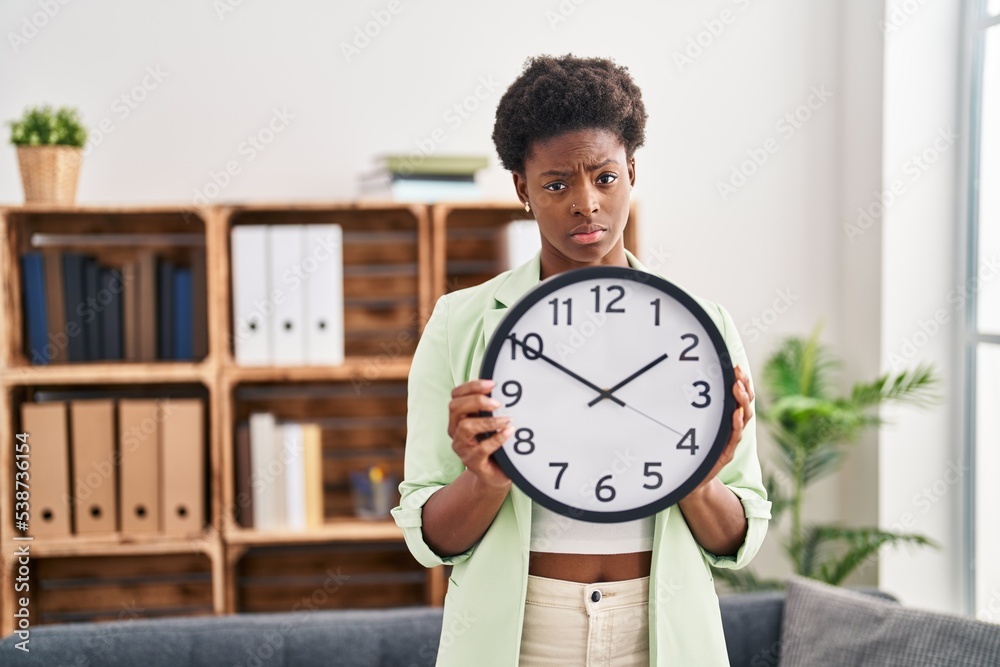 African american woman holding big clock skeptic and nervous, frowning upset because of problem. negative person. African american woman holding big clock skeptic and nervous, frowning upset because of problem. negative person.
