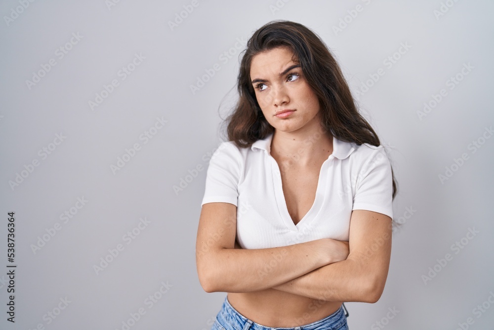 Young teenager girl standing over white background looking to the side with arms crossed convinced and confident Young teenager girl standing over white background looking to the side with arms crossed convinced and confident