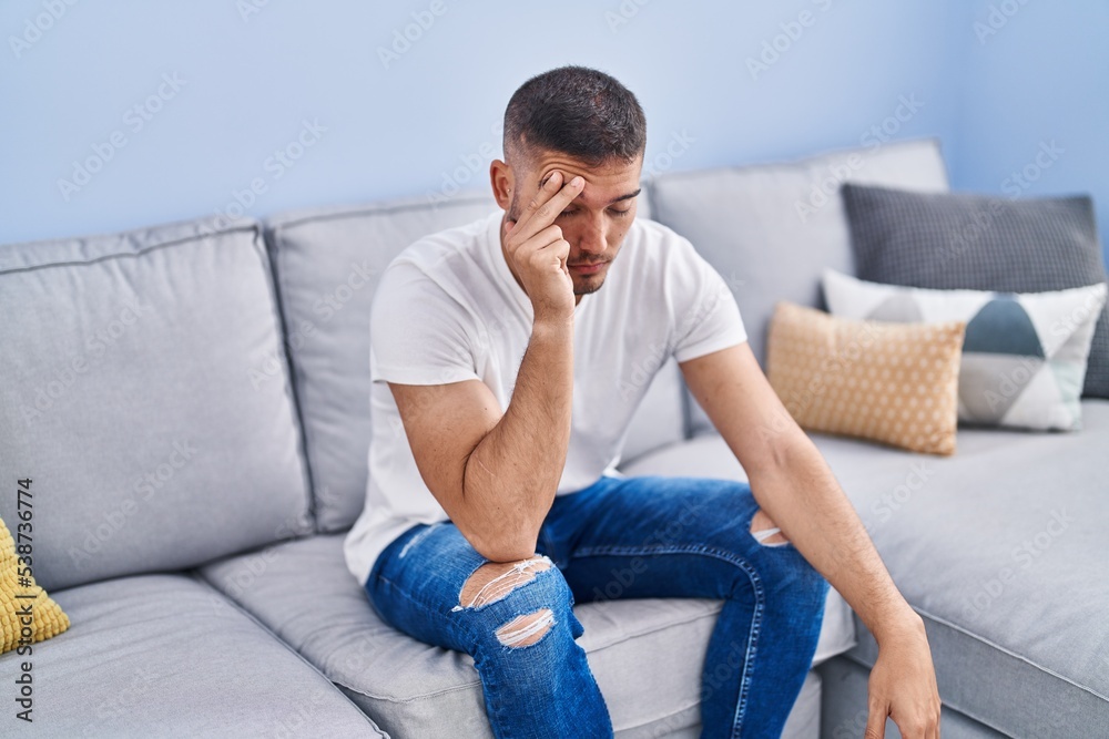 Young hispanic man stressed sitting on sofa at home