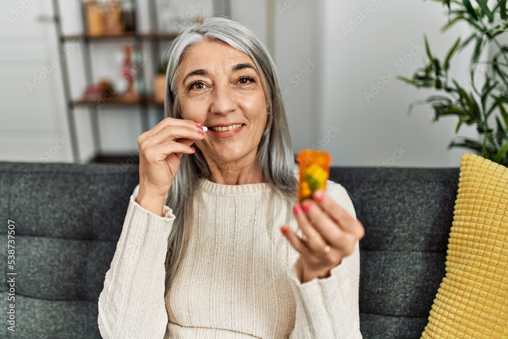 Middle age grey-haired woman smiling confident taking pills at home Middle age grey-haired woman smiling confident taking pills at home