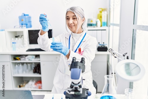 Middle age grey-haired woman wearing scientist uniform using pipette at laboratory