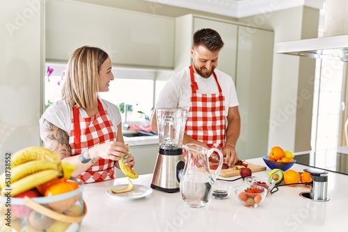 Young couple smiling confident making smoothie cooking at kitchen