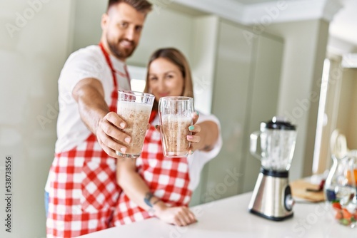 Young couple smiling confident holding glass of smoothie at kitchen