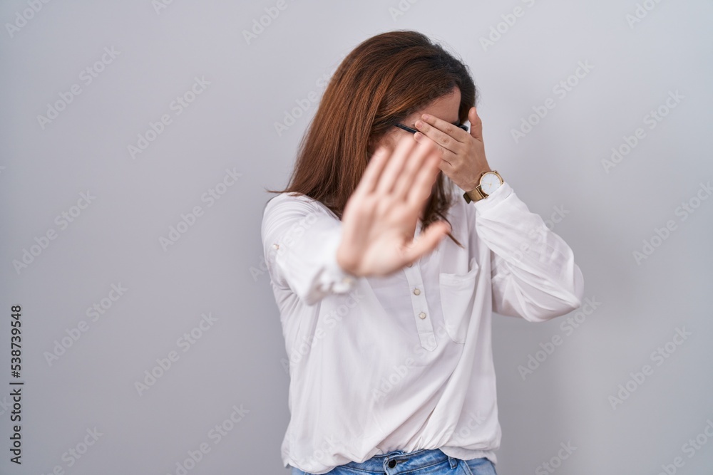 Brunette woman standing over white isolated background covering eyes with hands and doing stop gesture with sad and fear expression. embarrassed and negative concept. Brunette woman standing over white isolated background covering eyes with hands and doing stop gesture with sad and fear expression. embarrassed and negative concept.