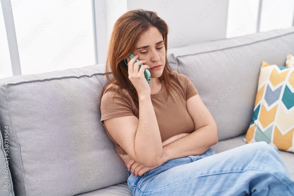 Young woman worried talking on smartphone sitting on sofa at home Young woman worried talking on smartphone sitting on sofa at home