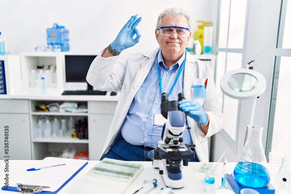 Senior caucasian man working at scientist laboratory smiling positive doing ok sign with hand and fingers. successful expression.