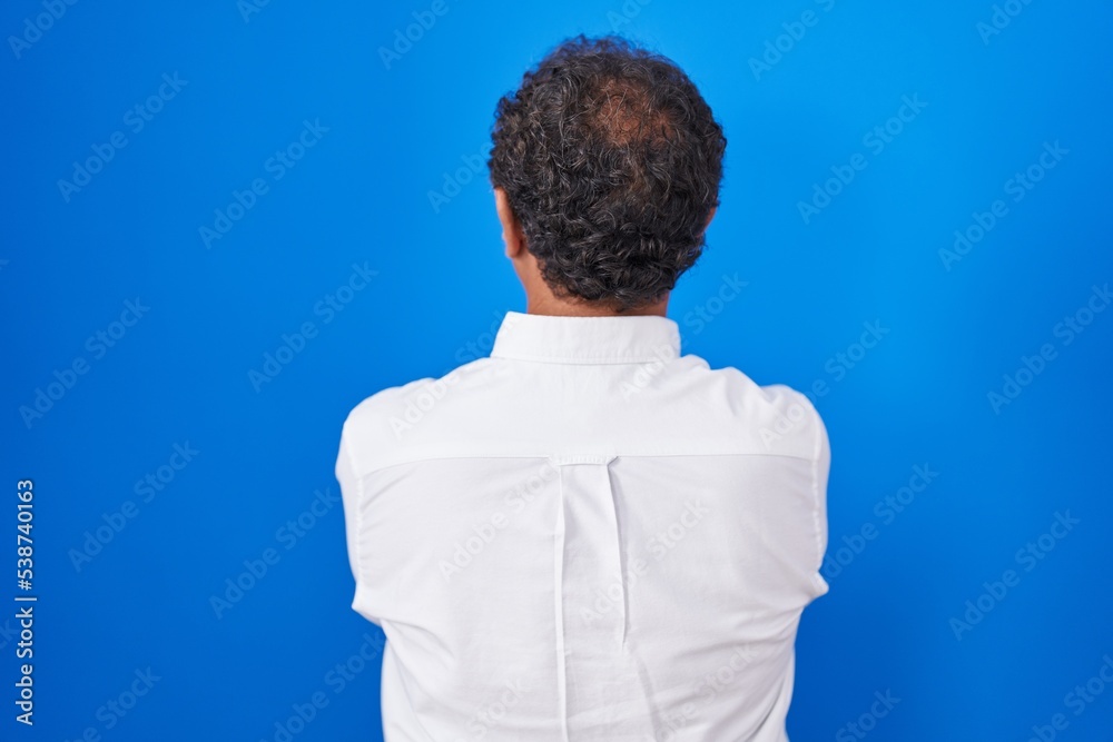 Middle age hispanic man standing over blue background standing backwards looking away with crossed arms Middle age hispanic man standing over blue background standing backwards looking away with crossed arms