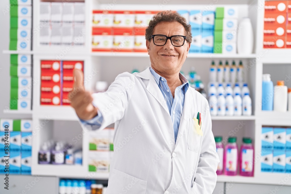Middle age man pharmacist smiling confident shake hand at pharmacy