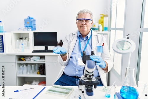 Senior caucasian man working at scientist laboratory pointing aside with hands open palms showing copy space  presenting advertisement smiling excited happy