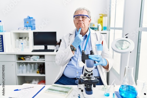 Senior caucasian man working at scientist laboratory thinking concentrated about doubt with finger on chin and looking up wondering