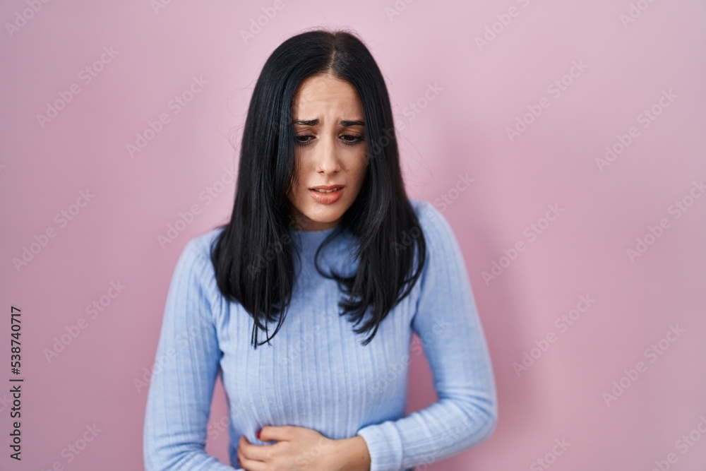 Hispanic woman standing over pink background with hand on stomach because indigestion, painful illness feeling unwell. ache concept. Hispanic woman standing over pink background with hand on stomach because indigestion, painful illness feeling unwell. ache concept.