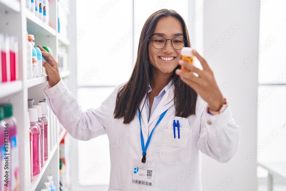 Young beautiful hispanic woman pharmacist smiling confident holding pills bottle at pharmacy Young beautiful hispanic woman pharmacist smiling confident holding pills bottle at pharmacy