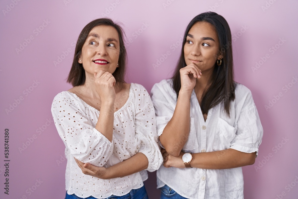 Hispanic mother and daughter together with hand on chin thinking about question, pensive expression. smiling and thoughtful face. doubt concept. Hispanic mother and daughter together with hand on chin thinking about question, pensive expression. smiling and thoughtful face. doubt concept.