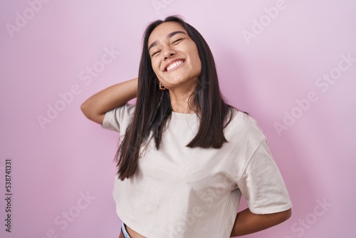 Young hispanic woman standing over pink background stretching back, tired and relaxed, sleepy and yawning for early morning