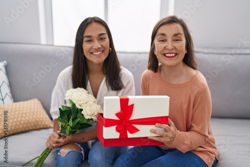 Two women mother and daughter holding flowers unpacking gift at home